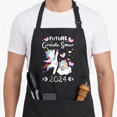 Tablier de cuisine noir avec une licorne blanche, un poney rose sur un nuage et le texte Future Grande Soeur 2024 entouré de cœurs roses.