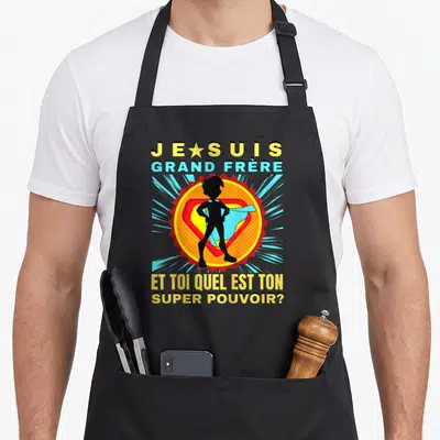 Tablier de cuisine noir avec silhouette super-héros et texte Je suis grand frère et toi quel est ton super pouvoir en jaune et bleu.