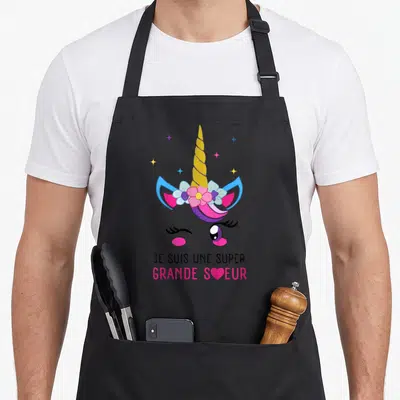 Tablier de cuisine noir avec illustration de licorne rose et texte Je suis une super grande sœur en bas.