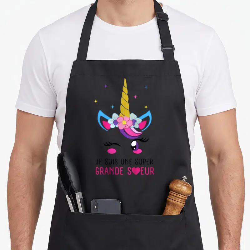 Tablier de cuisine noir avec illustration de licorne rose et texte Je suis une super grande sœur en bas.
