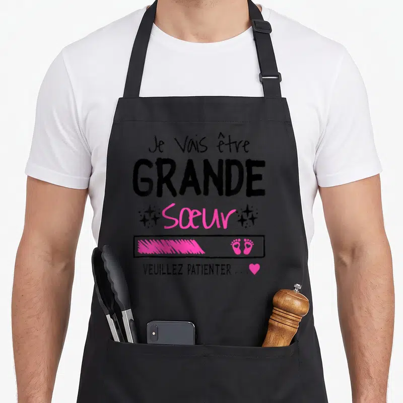 Tablier de cuisine noir avec inscription Je vais être grande sœur et petits pieds roses.