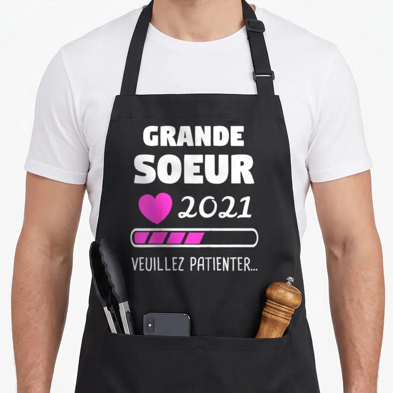 Tablier de cuisine noir avec inscription Grande Soeur 2021, cœur rose et barre de chargement.