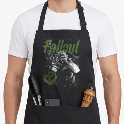 Tablier de cuisine noir avec illustration vert et gris représentant le casque Fallout et les symboles de la Confrérie de l'Acier.