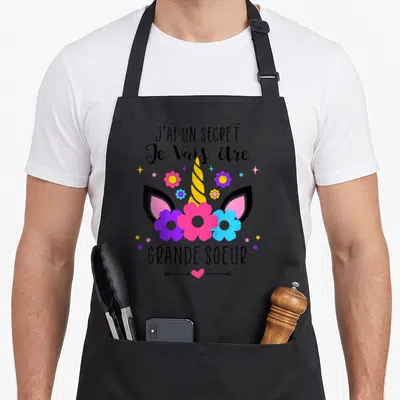 Tablier de cuisine noir avec illustration d'unicorne, fleurs et texte J'ai un secret Je Vais être Grande Soeur.