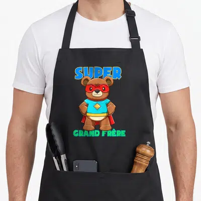 Tablier de cuisine noir avec ours en peluche masqué super-héros et texte SUPER GRAND FRÈRE coloré.