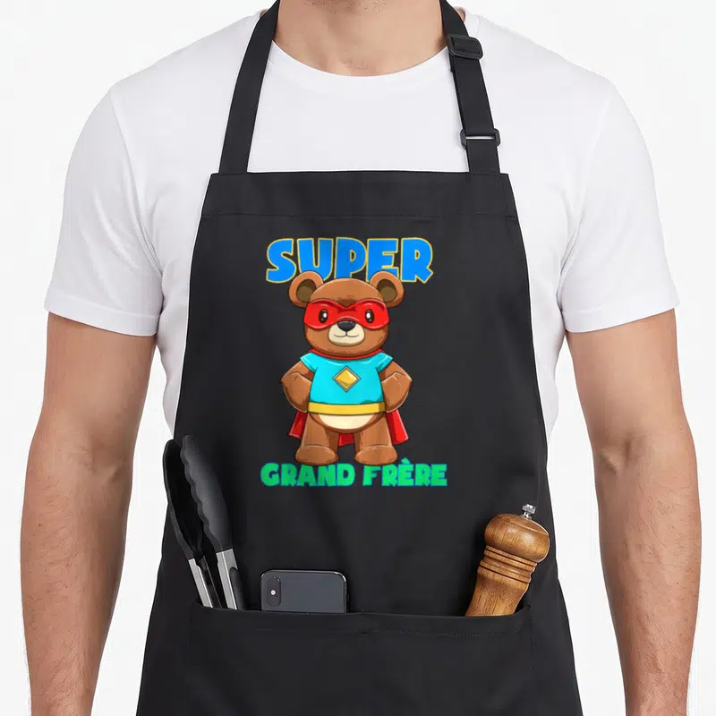 Tablier de cuisine noir avec ours en peluche masqué super-héros et texte SUPER GRAND FRÈRE coloré.