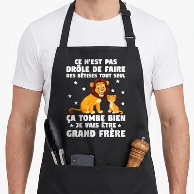 Tablier de cuisine noir avec un lion et un chaton entourés d'étoiles blanches sur fond sombre.