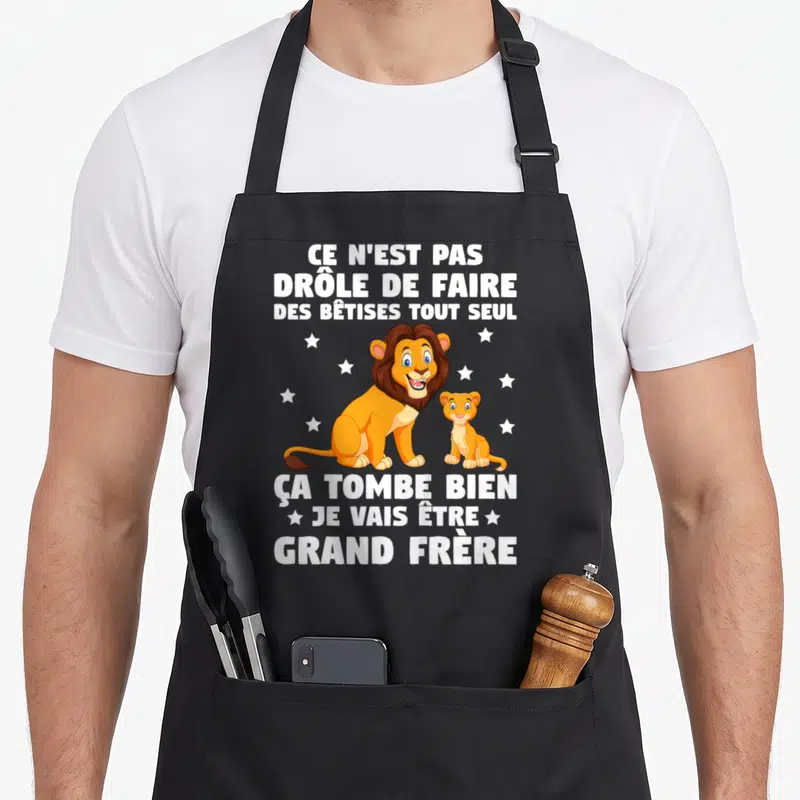 Tablier de cuisine noir avec un lion et un chaton entourés d'étoiles blanches sur fond sombre.