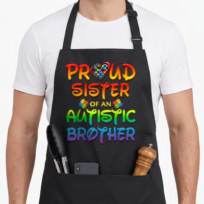 Tablier de cuisine noir avec inscription colorée PROUD SISTER OF AN AUTISTIC BROTHER et cœur en puzzle.
