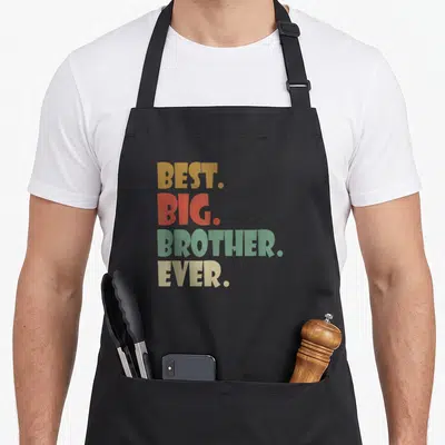 Tablier de cuisine noir avec l'inscription Best Big Brother Ever en typographie colorée et géométrique.