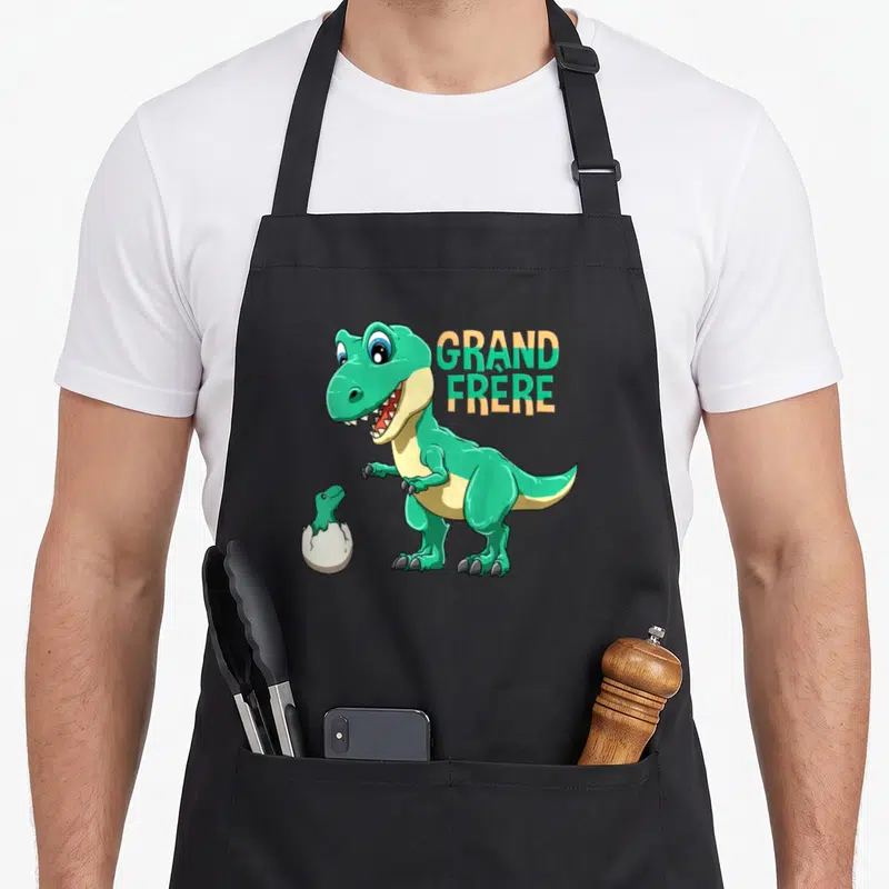 Tablier de cuisine noir avec un grand T-Rex vert et un bébé dinosaure sortant d'une coque.