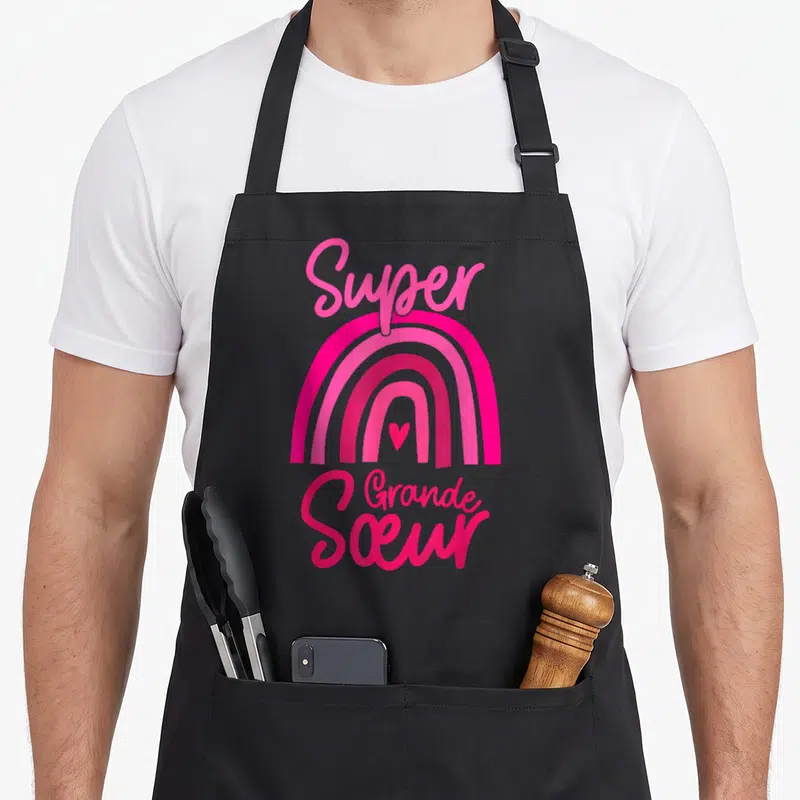 Tablier de cuisine noir avec arc-en-ciel rose et texte Super Grande Soeur en lettres cursives.