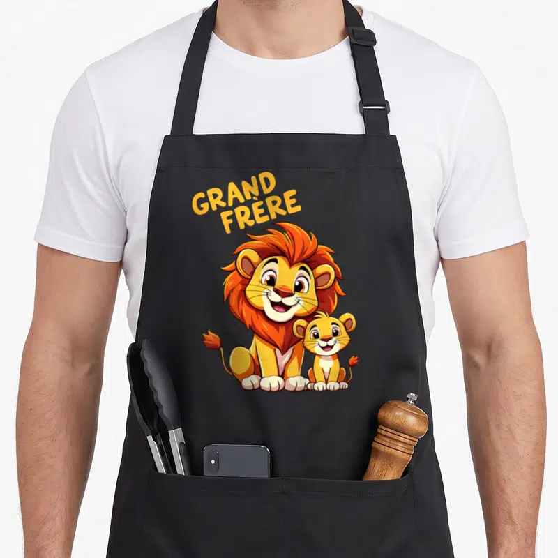 Tablier de cuisine noir avec un lion et un lionceau souriants sous l'inscription Grand Frère en lettres jaunes.