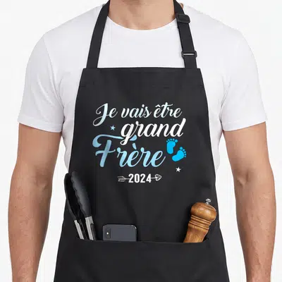 Tablier de cuisine noir avec inscription Je vais être grand Frère 2024 et deux petits pieds bleus.