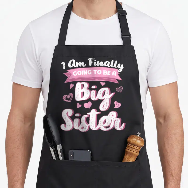 Tablier de cuisine noir avec inscription anglaise blanche et rose sur fond gris uni ornée de petits cœurs.