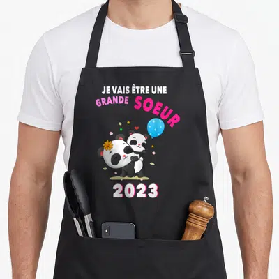 Tablier de cuisine noir avec deux pandas s'embrassant, un ballon bleu et le texte Je vais être une grande soeur 2023.