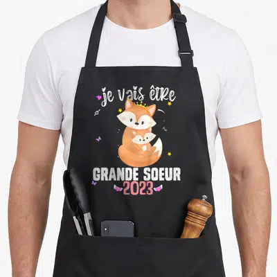 Tablier de cuisine noir avec un renard orange portant une couronne et tenant un petit renard, entouré d'étoiles et de cœurs roses.