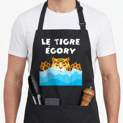 Tablier de cuisine noir avec un tigre cartoon sortant de l'eau et le texte Le Tigre Égory en lettres blanches au-dessus.