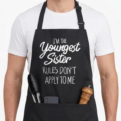 Tablier de cuisine noir avec l'inscription blanche I'm the youngest sister rules don't apply to me en style calligraphique.