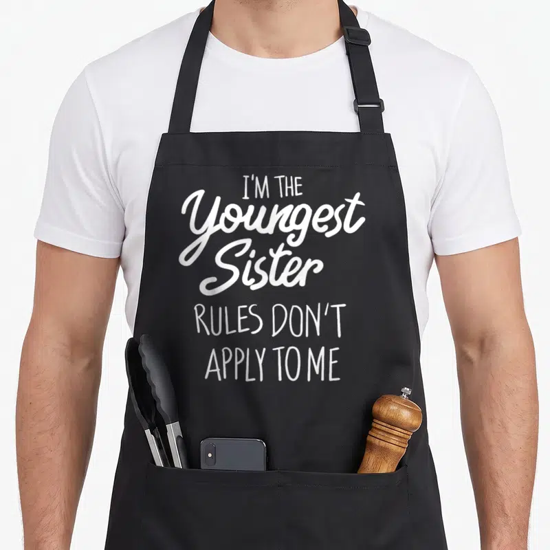 Tablier de cuisine noir avec l'inscription blanche I'm the youngest sister rules don't apply to me en style calligraphique.