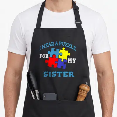 Tablier de cuisine noir avec quatre pièces de puzzle multicolores et texte bleu blanc soulignant le lien fraternel.