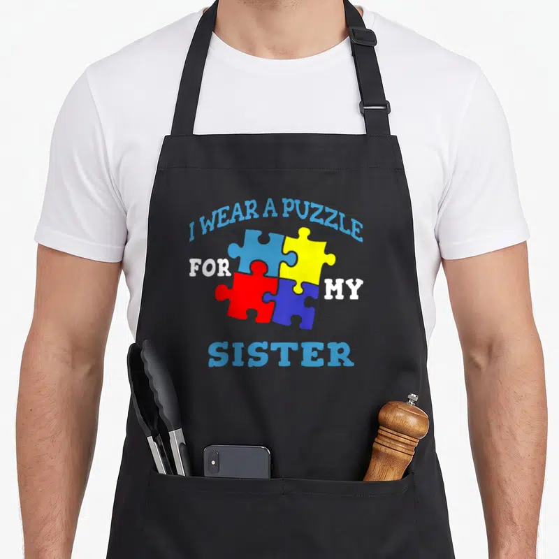 Tablier de cuisine noir avec quatre pièces de puzzle multicolores et texte bleu blanc soulignant le lien fraternel.