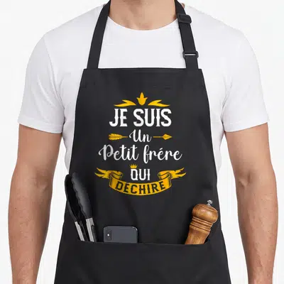 Tablier de cuisine noir avec inscription Je Suis Un Petit Frère Qui Déchire en blanc et jaune orné de couronnes et flèches.