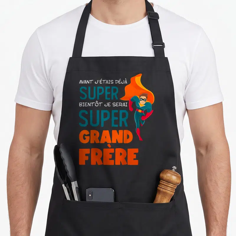Tablier de cuisine noir avec un super-héros volant et le texte super grand frère imprimé en bleu et orange.