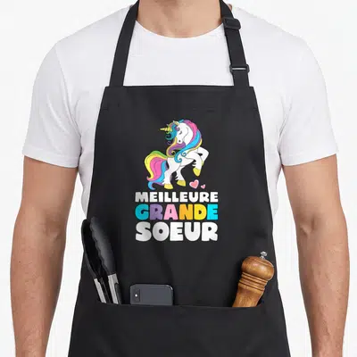 Tablier de cuisine noir avec une licorne colorée et le texte Meilleure Grande Soeur imprimé en lettres capitales.