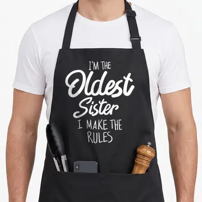 Tablier de cuisine noir avec inscription blanche I'm the Oldest Sister I make the rules en typographie mixte.