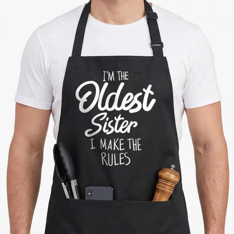 Tablier de cuisine noir avec inscription blanche I'm the Oldest Sister I make the rules en typographie mixte.