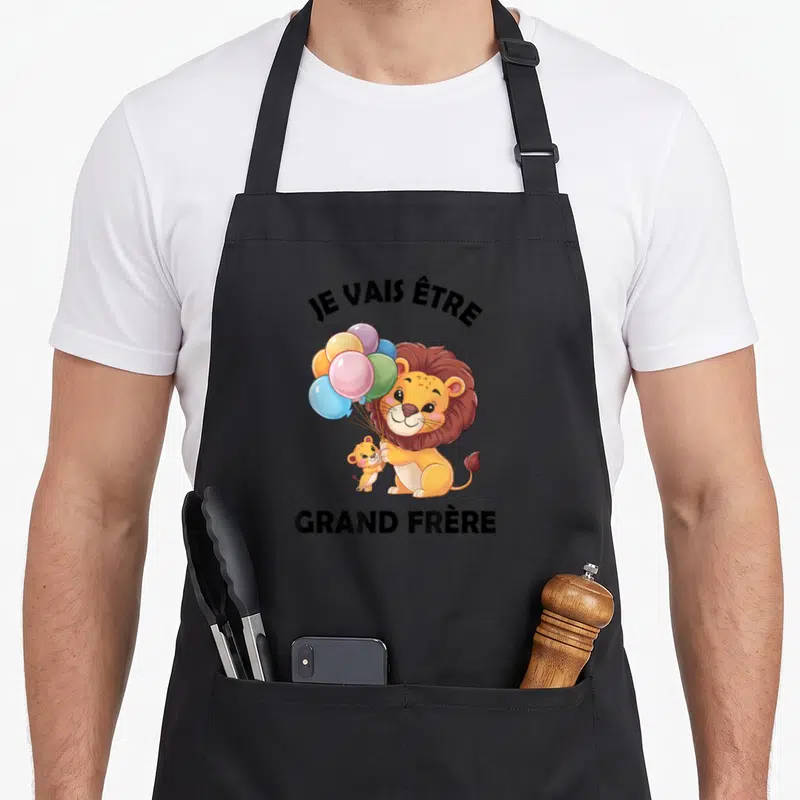 Tablier de cuisine noir avec illustration d'un lion tenant des ballons colorés et un petit lionceau à ses côtés.