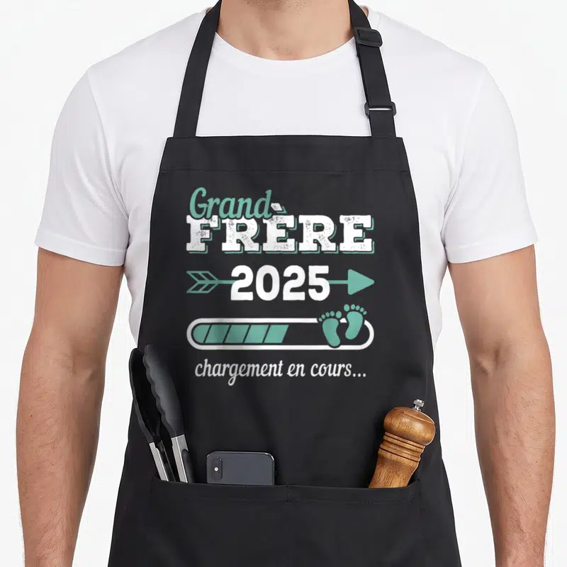 Tablier de cuisine noir avec texte blanc et vert indiquant grand frère 2025 chargement en cours avec des petits pieds.