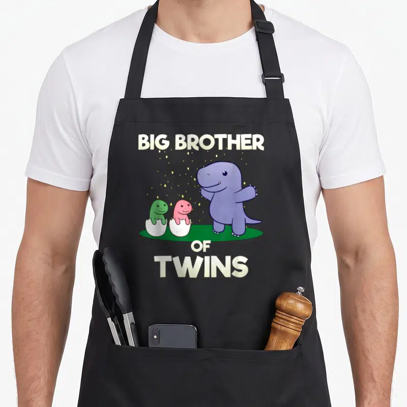 Tablier de cuisine noir avec illustration d'un dinosaure violet et deux bébés dinosaures vert et rose dans des coquilles d'œuf.