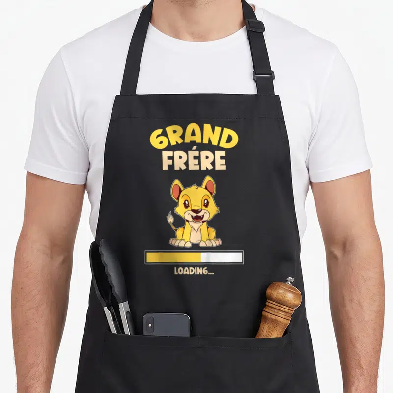 Tablier de cuisine noir avec un lion jaune et le texte Grand Frère Loading imprimé au centre.