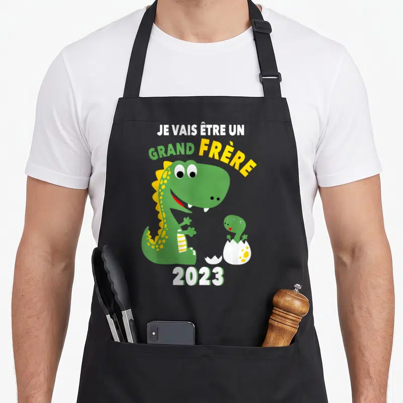 Tablier de cuisine noir avec un dinosaure vert et l'inscription Je vais être un grand frère 2023.