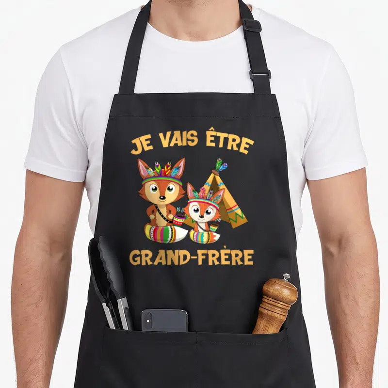 Tablier de cuisine noir avec deux renards en tenue amérindienne et le texte Je vais être grand-frère imprimé en orange.