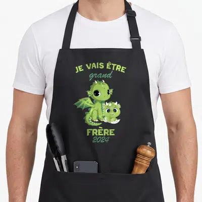 Tablier de cuisine noir avec deux dragons verts et le texte Je vais être grand frère 2024 imprimé au centre.