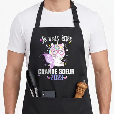 Tablier de cuisine noir avec une licorne rose et l'inscription je vais être grande sœur 2023.