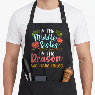 Tablier de cuisine noir avec inscription sœur intermédiaire raison règles et décorations florales roses et vertes.