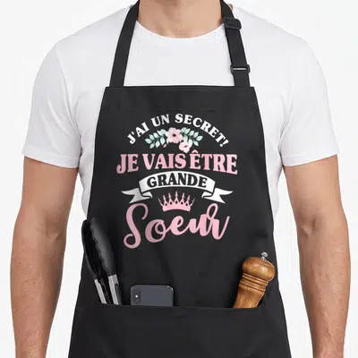 Tablier de cuisine noir avec inscription J'ai un secret je vais être grande soeur et couronne rose.