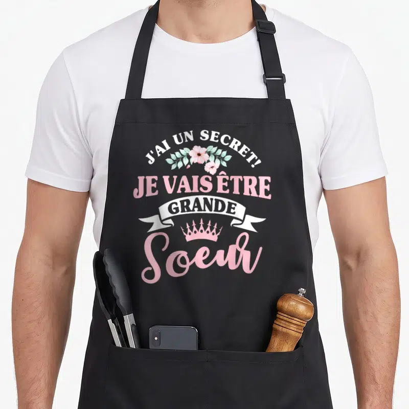 Tablier de cuisine noir avec inscription J'ai un secret je vais être grande soeur et couronne rose.