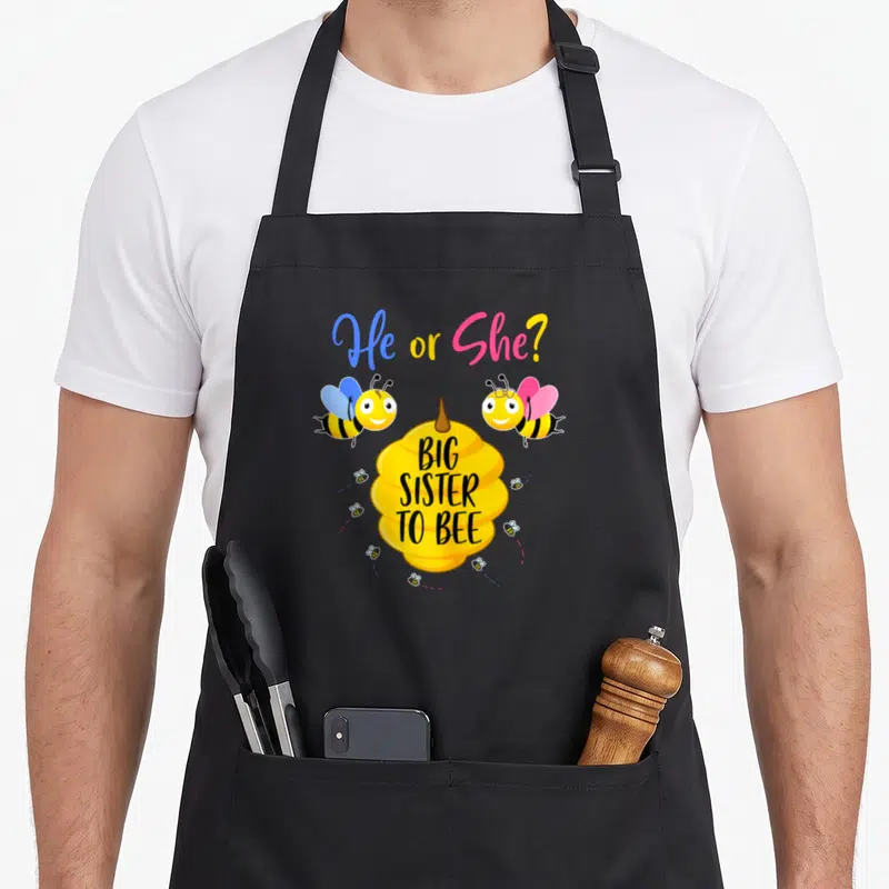 Tablier de cuisine noir avec une ruche jaune, deux abeilles colorées et le texte He or She Big Sister to Bee.