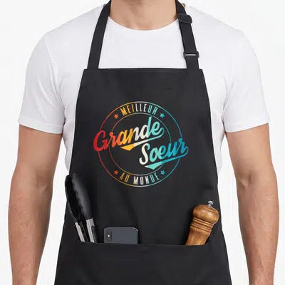 Tablier de cuisine noir avec logo circulaire coloré Meilleur Grande Soeur au Monde et étoiles décoratives.