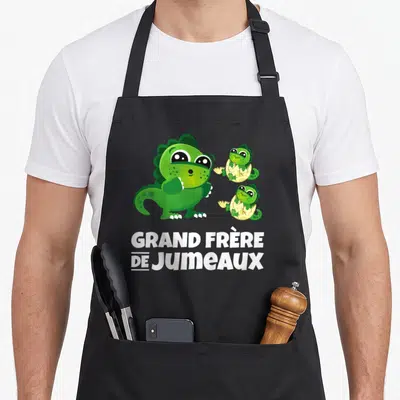 Tablier de cuisine noir avec trois dinosaures verts et l'inscription GRAND FRÈRE DE JUMEAUX en blanc.