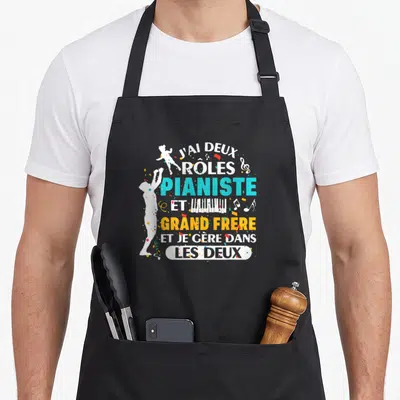 Tablier de cuisine noir avec silhouette pianiste et texte J'ai deux rôles pianiste et grand frère en couleurs vives.