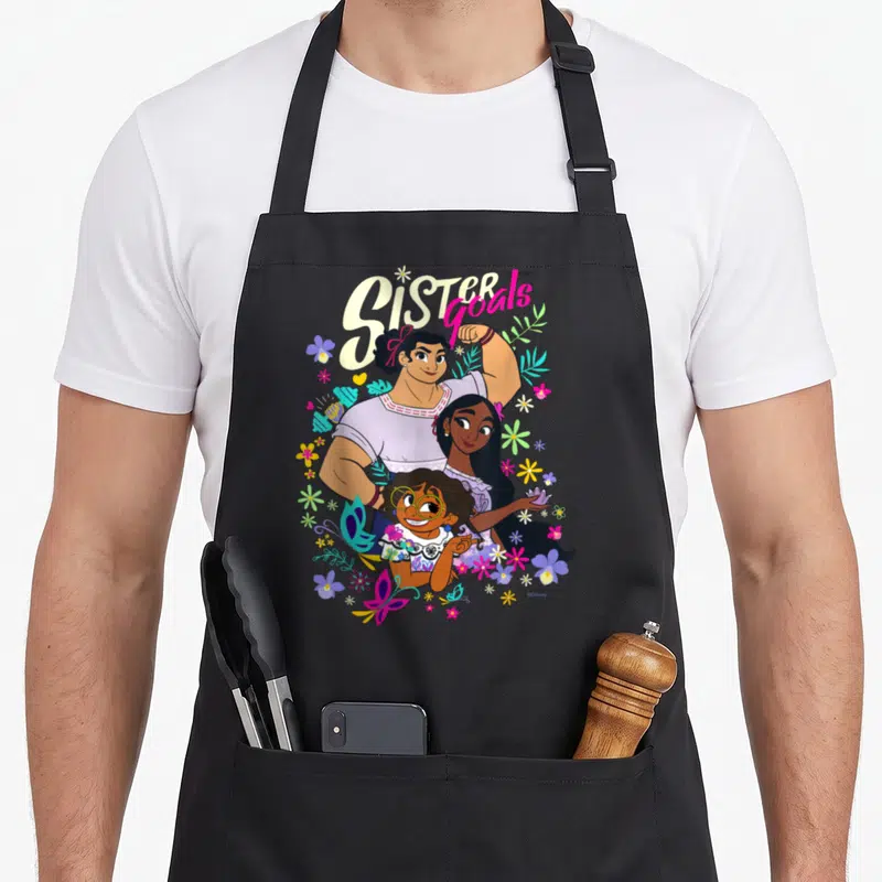 Tablier de cuisine noir avec illustration colorée Mirabel Isabela Luisa Sister Goals et motifs floraux.