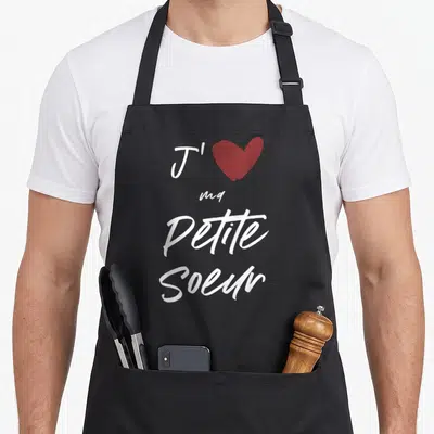 Tablier de cuisine noir avec l'inscription J'aime ma petite sœur et un cœur rouge stylisé en haut du motif.