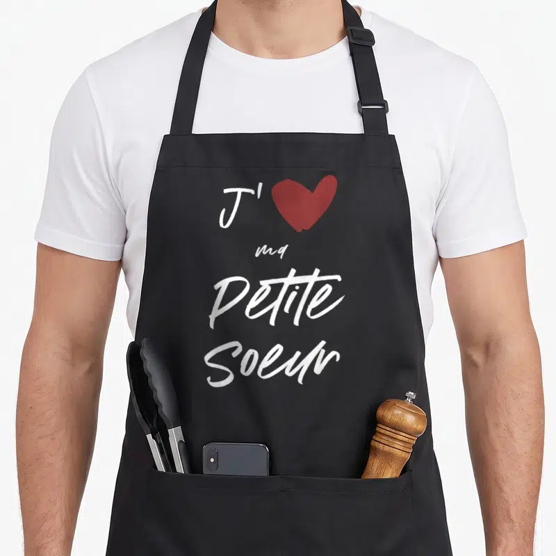 Tablier de cuisine noir avec l'inscription J'aime ma petite sœur et un cœur rouge stylisé en haut du motif.