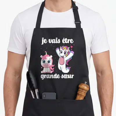 Tablier de cuisine noir avec deux licornes roses et le texte je vais être grande sœur en lettres blanches.